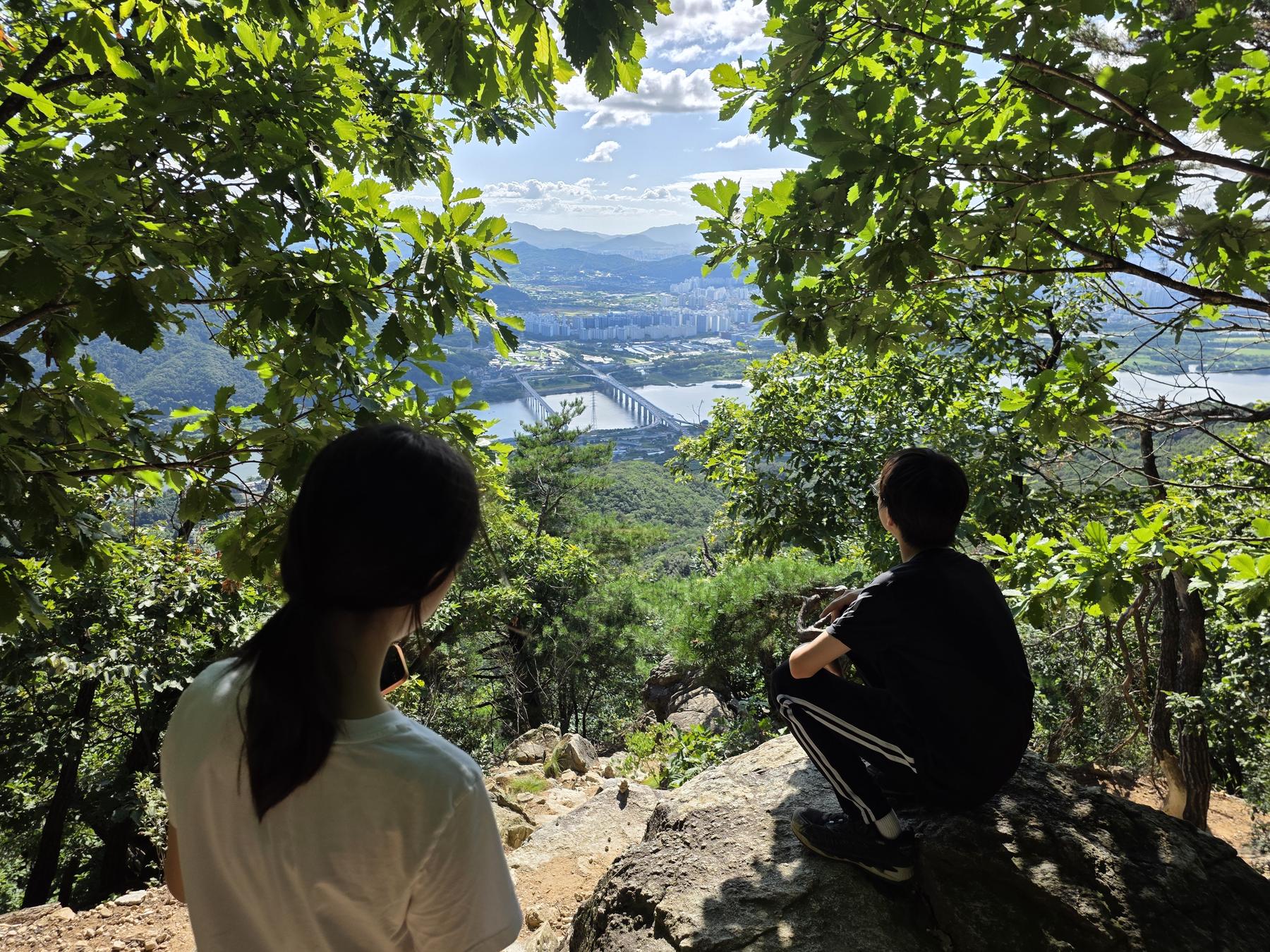 바위에 앉아 산 아래 강과 도시를 내려다보는 두 학생